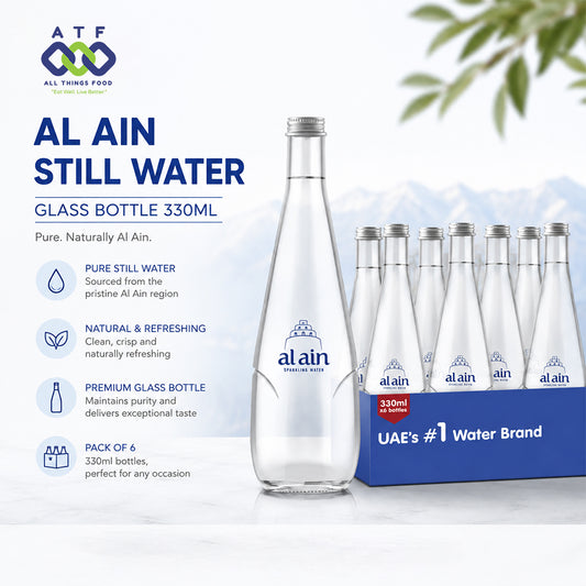 A clear glass water bottle and a matching pack of six Al Ain Still Water 330ml glass bottles in a blue cardboard case with promotional text and a faint mountain graphic.