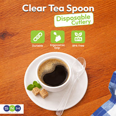 Clear tea spoon on a saucer with a cup of tea, placed on a wooden surface.