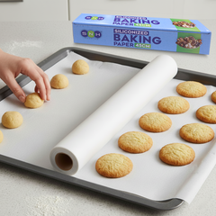 Baking sheet with cookies and a roll of baking paper, with a box of baking paper in the background.