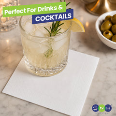 Cocktail glass with lemon and rosemary garnish on a marble surface, with 'SNH' branding.